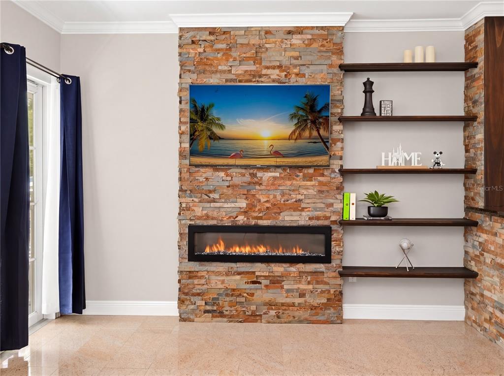 A living room features a stone fireplace wall with a mounted television and open shelving — 709 BLOOM STREET UNIT 160, CELEBRATION, FL