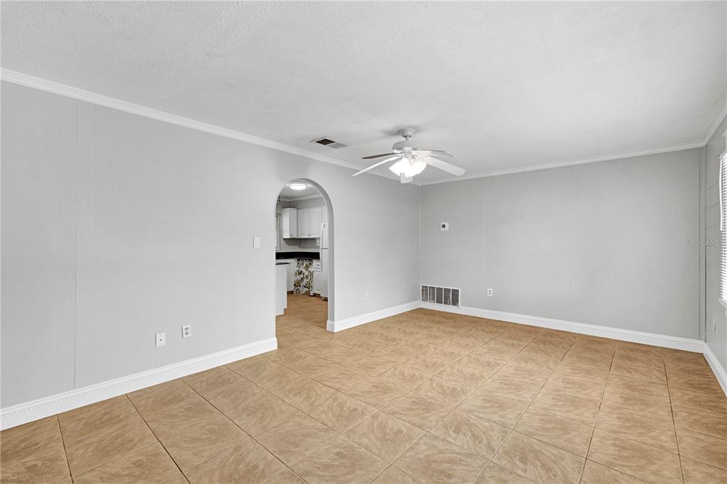 An empty room with light gray walls, tan tile flooring, and an arched kitchen doorway — 4314 LARK DRIVE, DOVER, FL