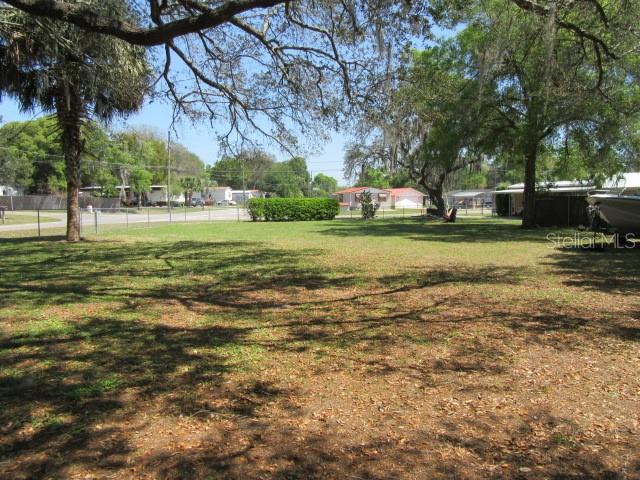 A grassy, tree-shaded residential lot with a chain-link fence and neighboring houses in the background — SE 102ND COURT RD, SUMMERFIELD, FL