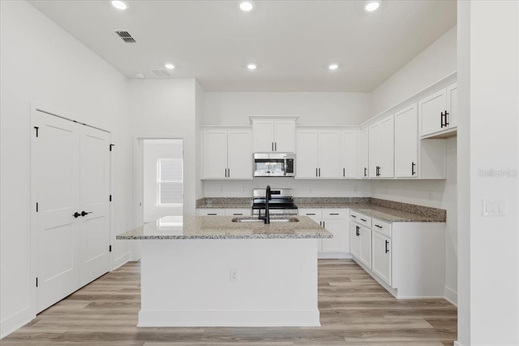 A kitchen with white cabinets, granite countertops, a center island, and light wood-look flooring — 13658 NW 150TH CIRCLE, ALACHUA, FL