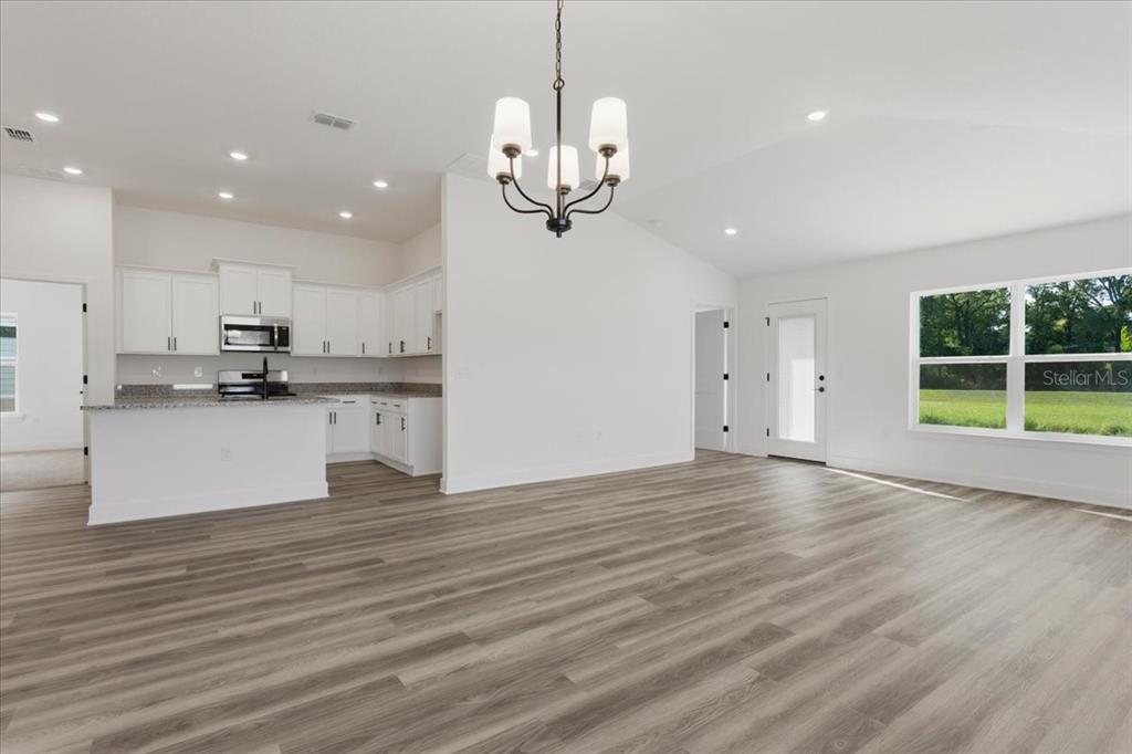 An open-concept living area features white cabinets, granite countertops, and light wood-look flooring — 13658 NW 150TH CIRCLE, ALACHUA, FL