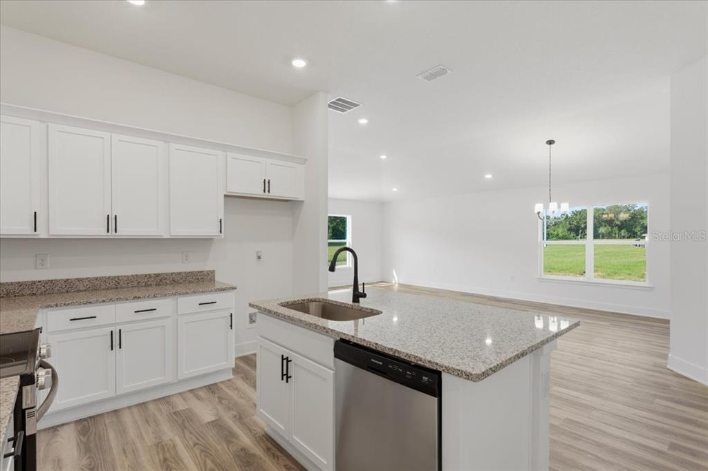 A kitchen with white cabinets, granite countertops, and a center island overlooks an open living area — 13658 NW 150TH CIRCLE, ALACHUA, FL