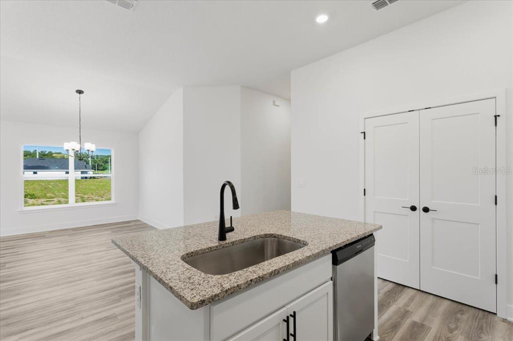A kitchen island with a granite countertop and sink faces a dining area with windows — 13658 NW 150TH CIRCLE, ALACHUA, FL