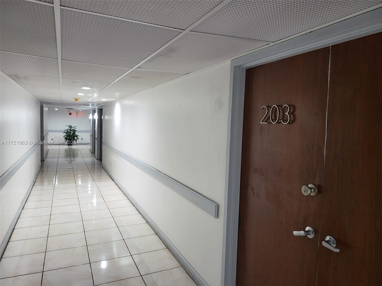 A hallway with white tiled floors and a wooden door labeled 203 — 13499 Biscayne Blvd, North Miami FL 33181, NORTH MIAMI, FL