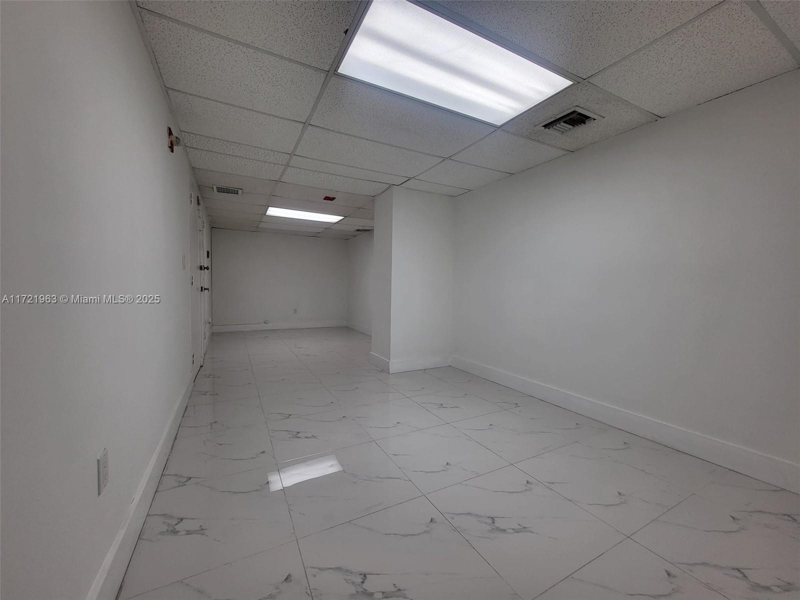 An empty, white-walled room features a drop ceiling with recessed lighting and marble-patterned tile flooring — 13499 Biscayne Blvd, North Miami FL 33181, NORTH MIAMI, FL