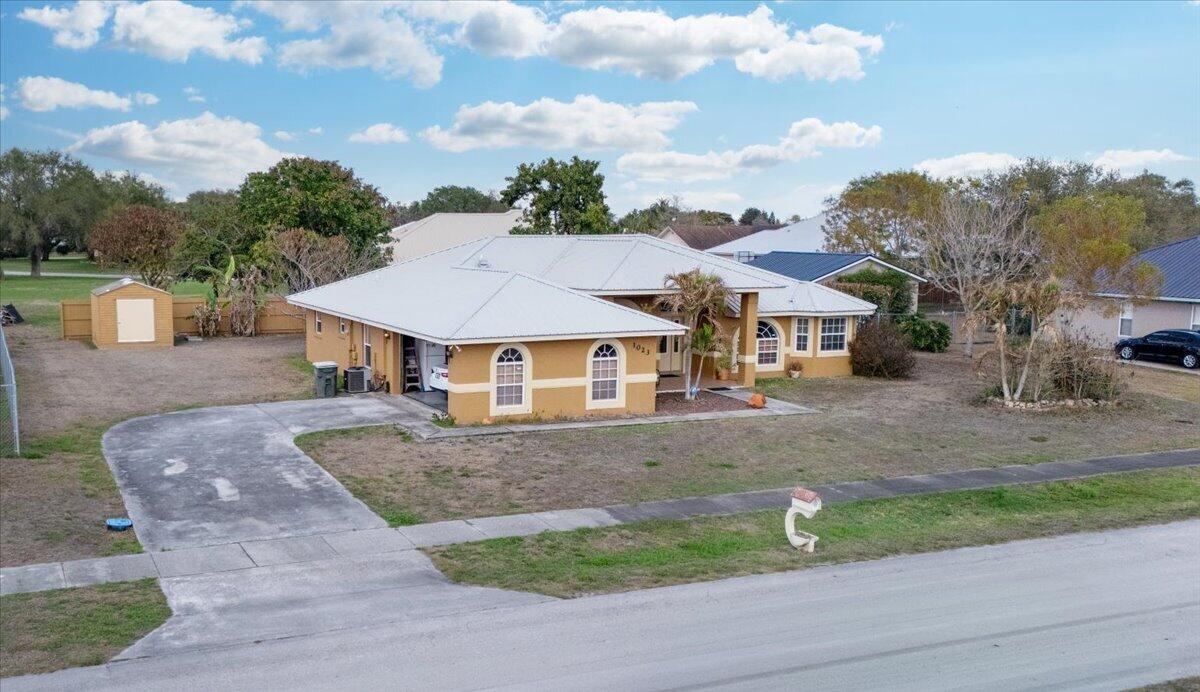 A single-story, tan-colored house with a white metal roof sits on a large grassy lot — 1023 Caribbean Avenue, Clewiston FL 33440, CLEWISTON, FL