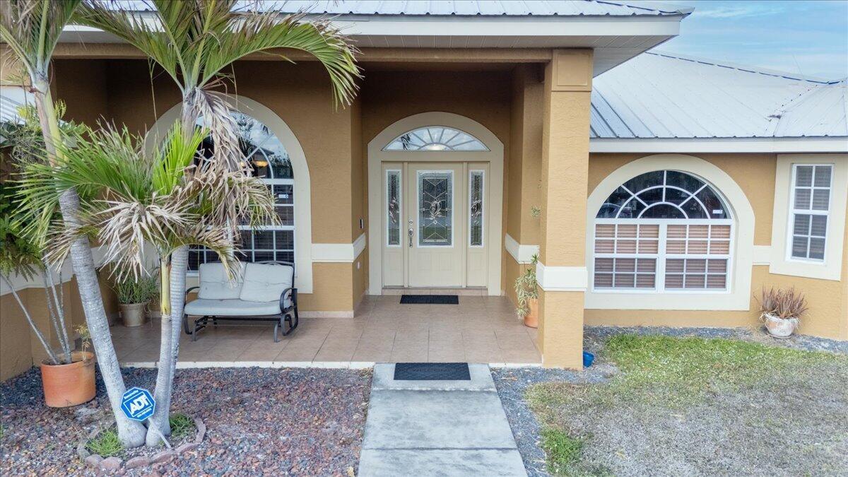 The exterior of a tan house features a covered entryway, arched windows, and a palm tree — 1023 Caribbean Avenue, Clewiston FL 33440, CLEWISTON, FL