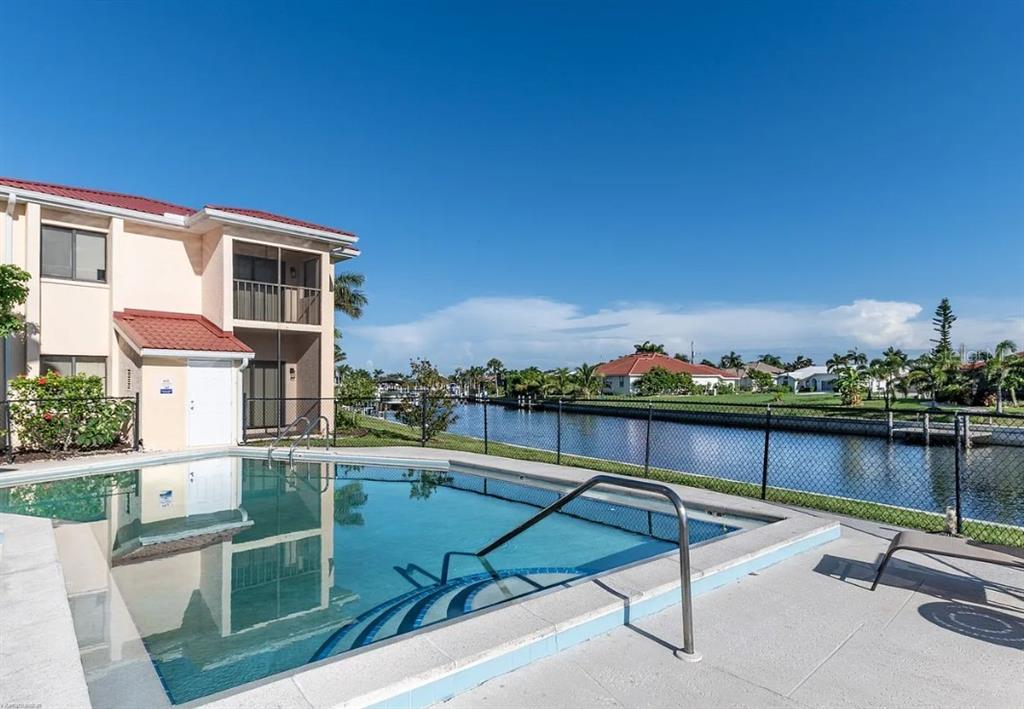A swimming pool sits on a patio next to a two-story building and a canal — 1204 SPANISH CAY LANE UNIT A, PUNTA GORDA, FL