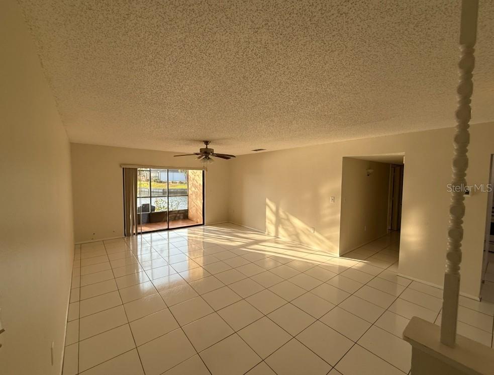 An empty living room with white tile floors, a ceiling fan, and a sliding glass door — 1204 SPANISH CAY LANE UNIT A, PUNTA GORDA, FL