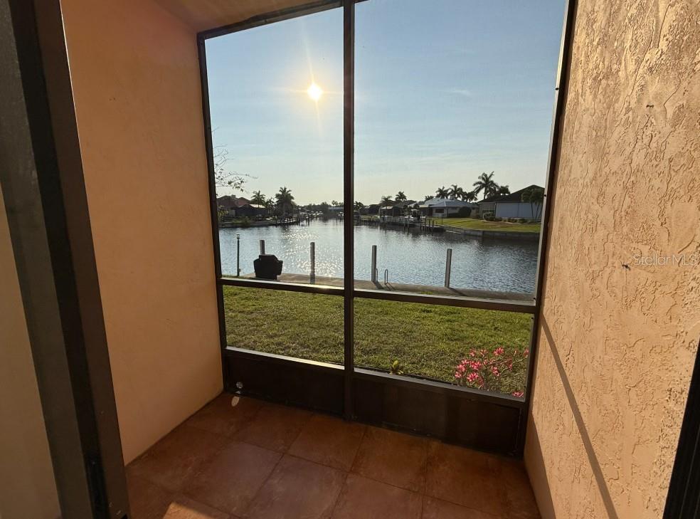 A screened-in porch with tile flooring overlooks a canal and residential waterfront properties — 1204 SPANISH CAY LANE UNIT A, PUNTA GORDA, FL