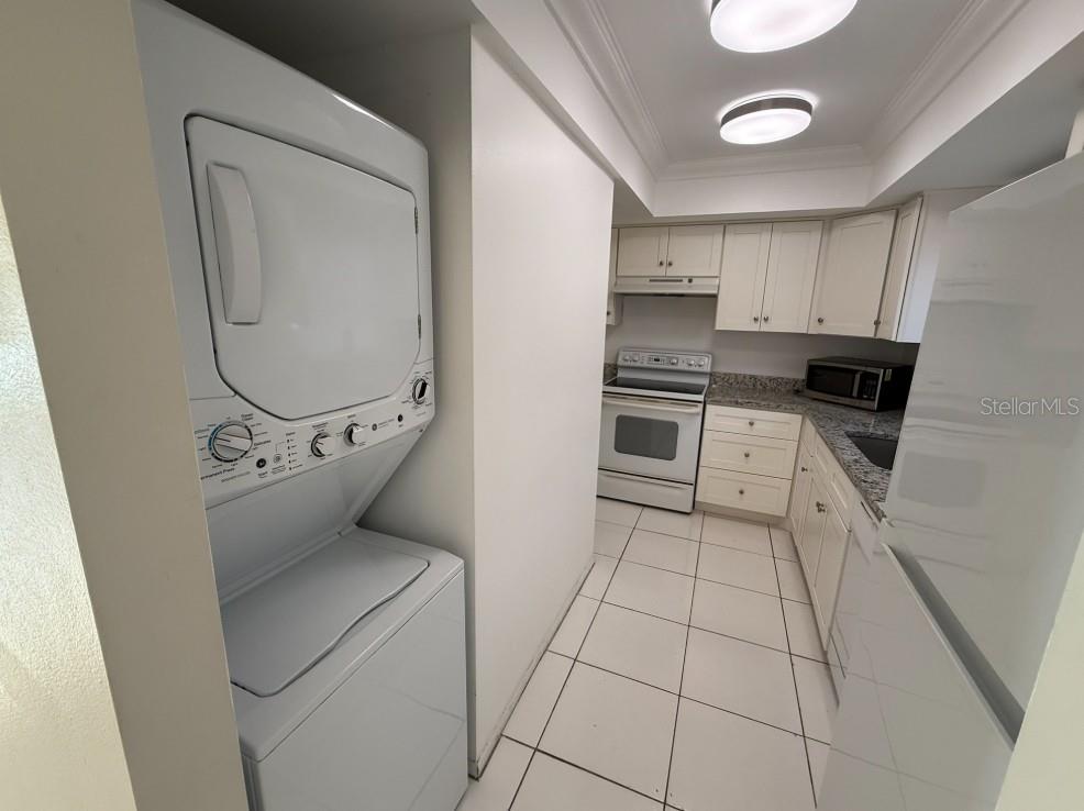 A kitchen features white cabinets, granite countertops, tile flooring, and a stacked washer and dryer — 1204 SPANISH CAY LANE UNIT A, PUNTA GORDA, FL