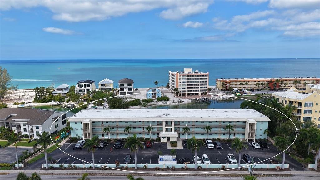 An aerial view shows a multi-story, light blue apartment building with a parking lot — 9200 MIDNIGHT PASS ROAD UNIT 25, SARASOTA, FL