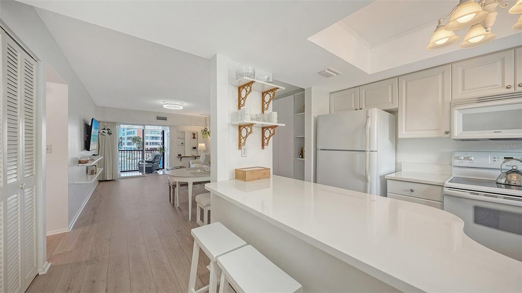 A white kitchen with a breakfast bar overlooks a dining area and a balcony — 9200 MIDNIGHT PASS ROAD UNIT 25, SARASOTA, FL