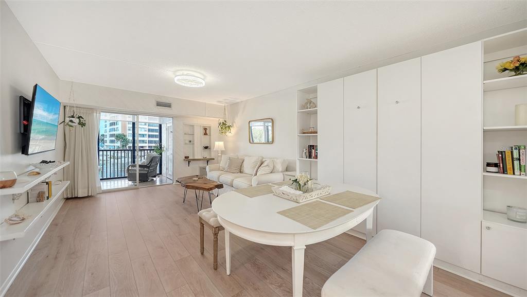 A bright living and dining area features light wood floors, white cabinetry, and a balcony — 9200 MIDNIGHT PASS ROAD UNIT 25, SARASOTA, FL