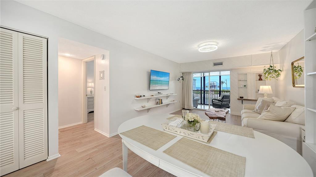 A bright living and dining area features light wood floors, white walls, and balcony access — 9200 MIDNIGHT PASS ROAD UNIT 25, SARASOTA, FL