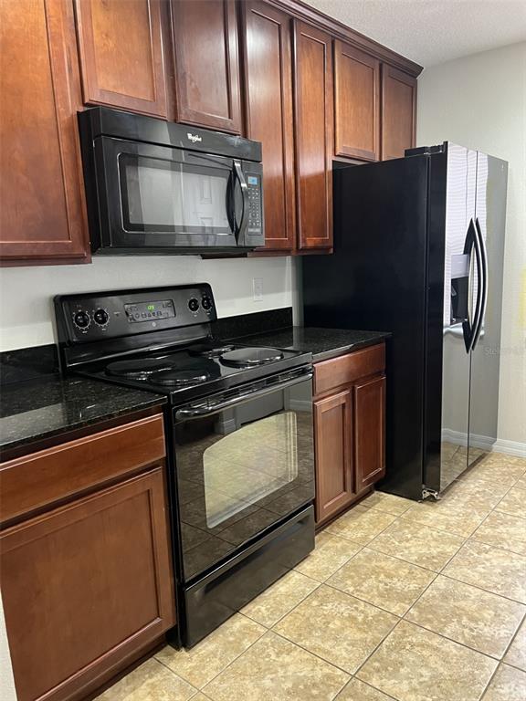 A kitchen features dark wood cabinets, black appliances, and black granite countertops over tiled floors — 5444 RIVER ROCK ROAD, LAKELAND, FL