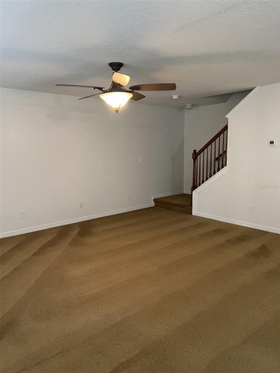 A living room with tan carpet, a ceiling fan, and a staircase with wooden railings — 5444 RIVER ROCK ROAD, LAKELAND, FL