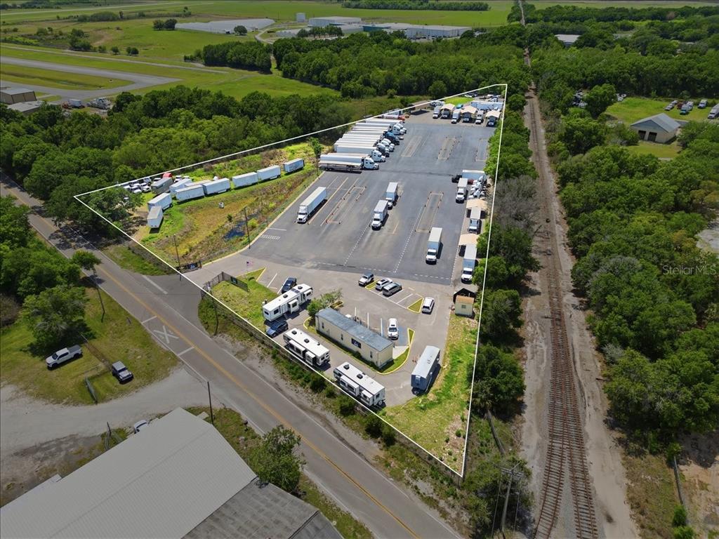 An aerial view shows a triangular lot with a parking area, trailers, and buildings — 100 S AIRPORT ROAD, LAKE WALES, FL