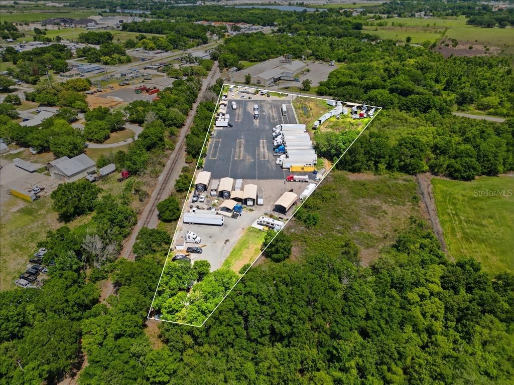 An aerial view shows a triangular industrial lot with parked semi-trucks and small structures — 100 S AIRPORT ROAD, LAKE WALES, FL