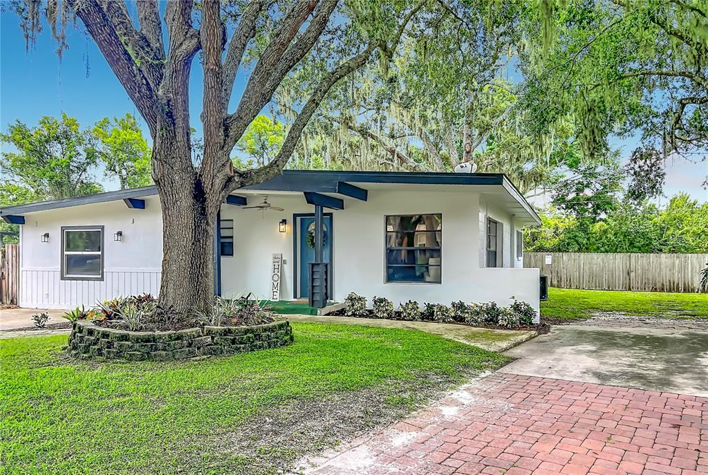 A white single-story house with a large tree in the front yard and brick driveway — 719 CHEROKEE CIRCLE, SANFORD, FL