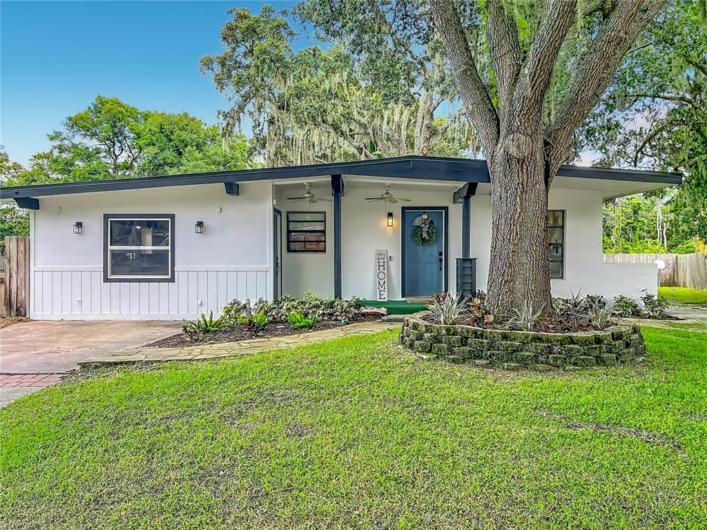 A single-story white house with a blue front door and a large tree in front — 719 CHEROKEE CIRCLE, SANFORD, FL