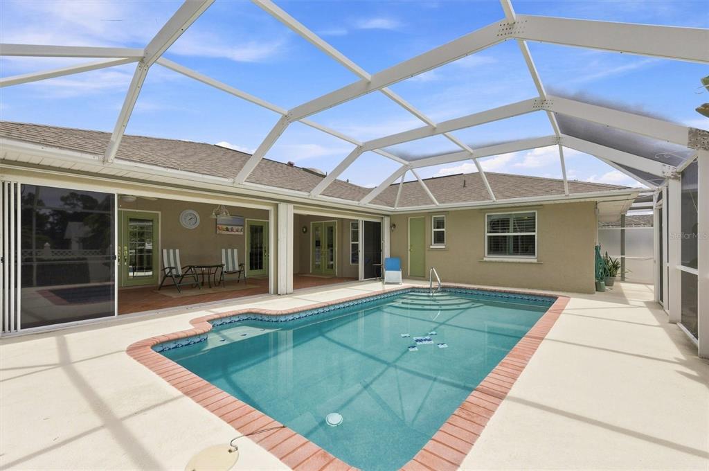 A screened-in swimming pool with a brick border sits on a patio behind a house — 317 SALVADOR DRIVE, PUNTA GORDA, FL