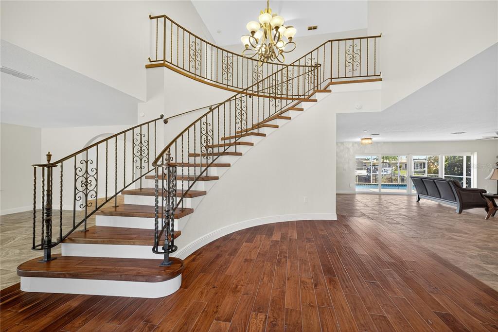 A grand curved staircase with ornate metal railings stands in a spacious, light-filled foyer — 5124 SOUTH SHORE DRIVE, NEW PORT RICHEY, FL