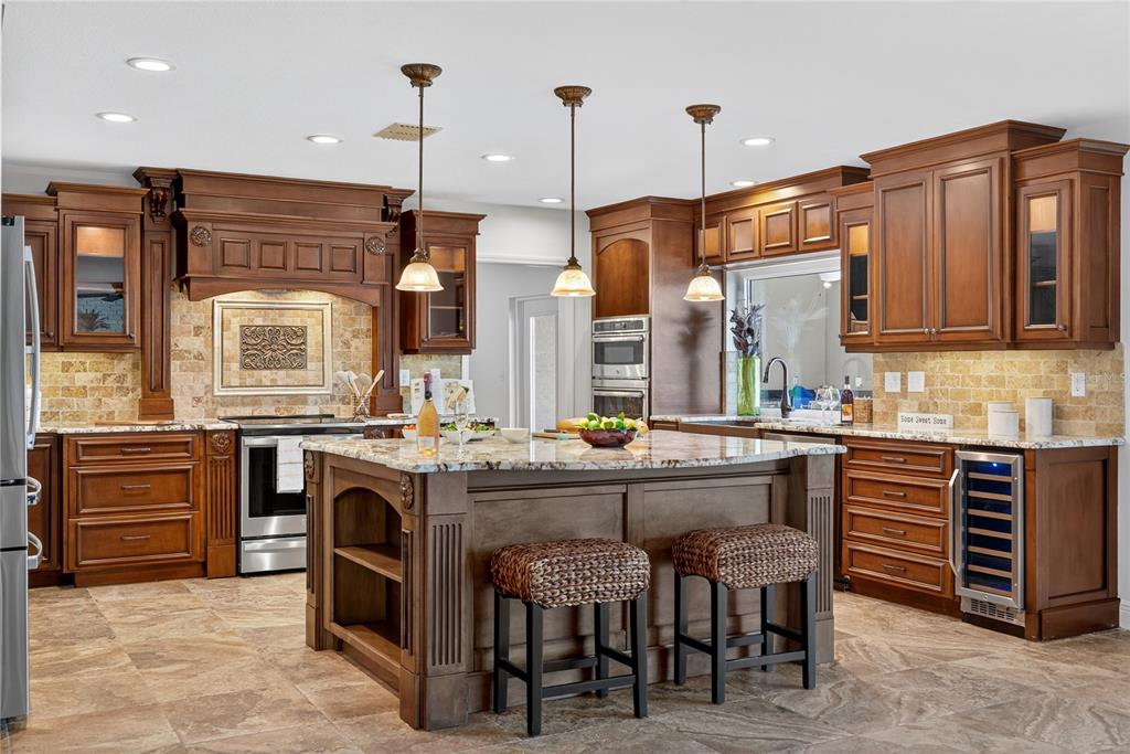 A kitchen features dark wood cabinets, a large granite-topped island, and stone tile flooring — 5124 SOUTH SHORE DRIVE, NEW PORT RICHEY, FL
