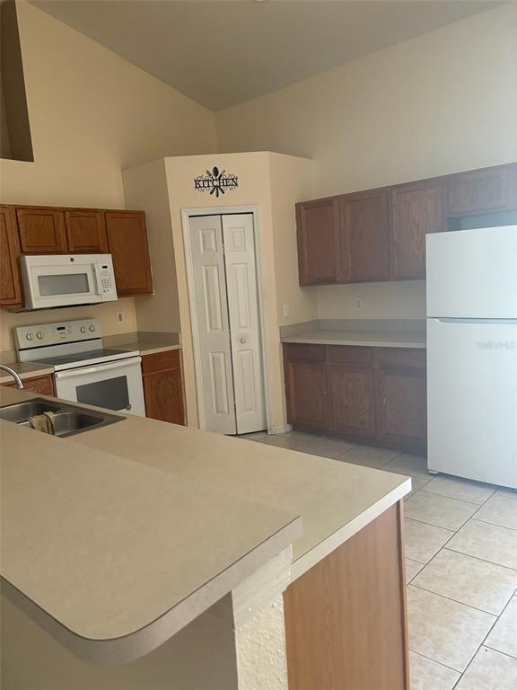 A kitchen features wood cabinets, white appliances, a breakfast bar, and light-colored tile flooring — 673 COTULLA DRIVE, KISSIMMEE, FL