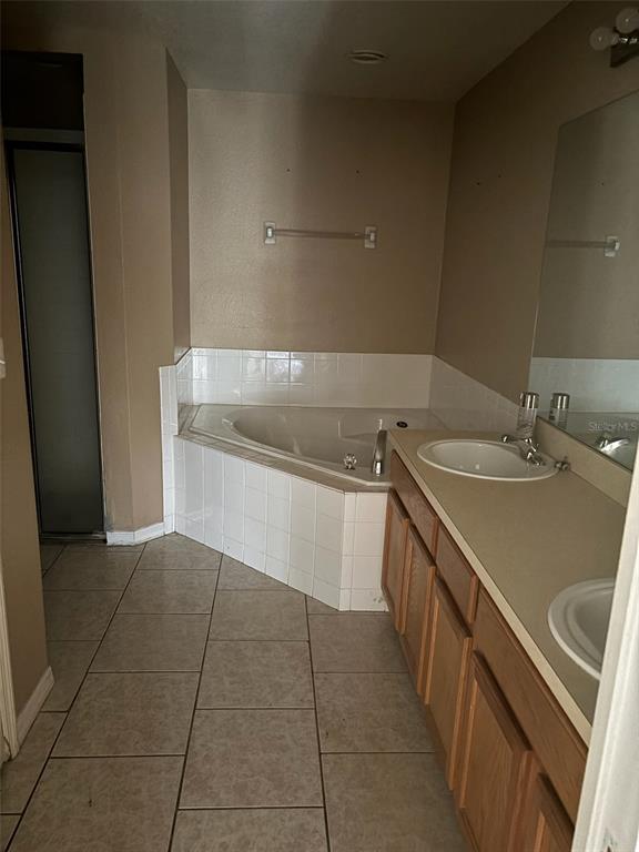 A bathroom features a corner soaking tub, a double vanity, and light-colored tile flooring — 673 COTULLA DRIVE, KISSIMMEE, FL