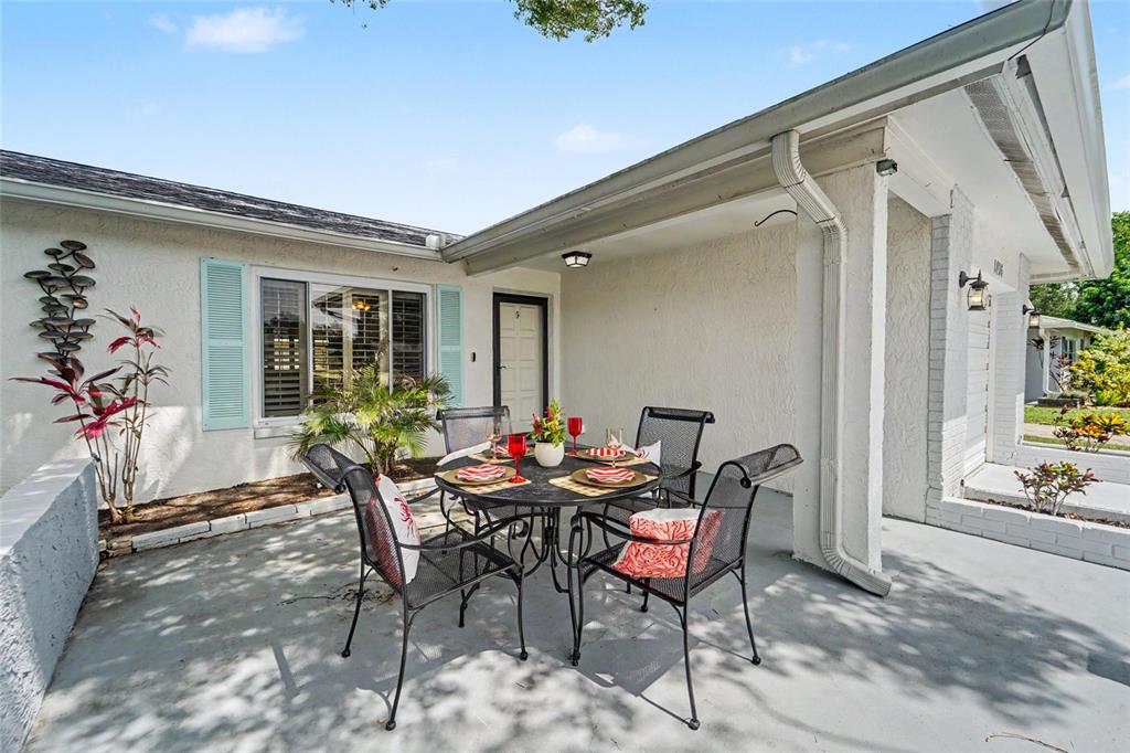 A patio features a round metal dining set with four chairs against a white house — 1496 QUEEN ANNE DRIVE, PALM HARBOR, FL