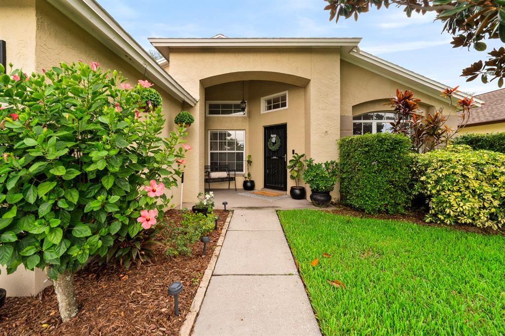 A concrete walkway leads to the front entrance of a tan house with landscaping — 1518 WESTERLY DRIVE, BRANDON, FL