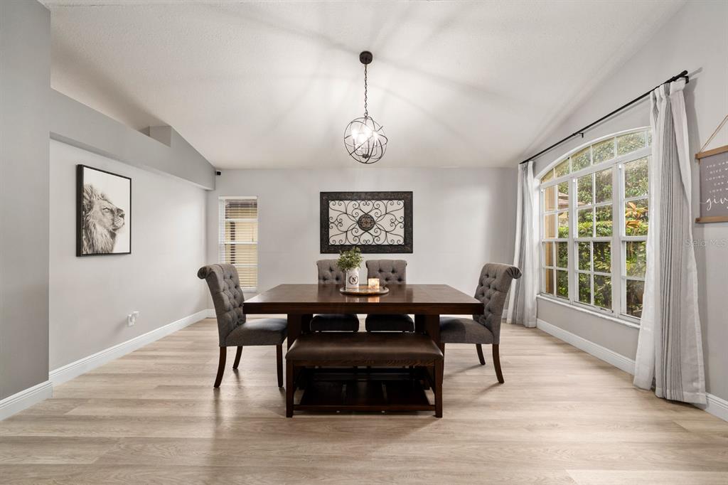 A dining room features a wooden table, gray tufted chairs, a bench, and a globe chandelier — 1518 WESTERLY DRIVE, BRANDON, FL