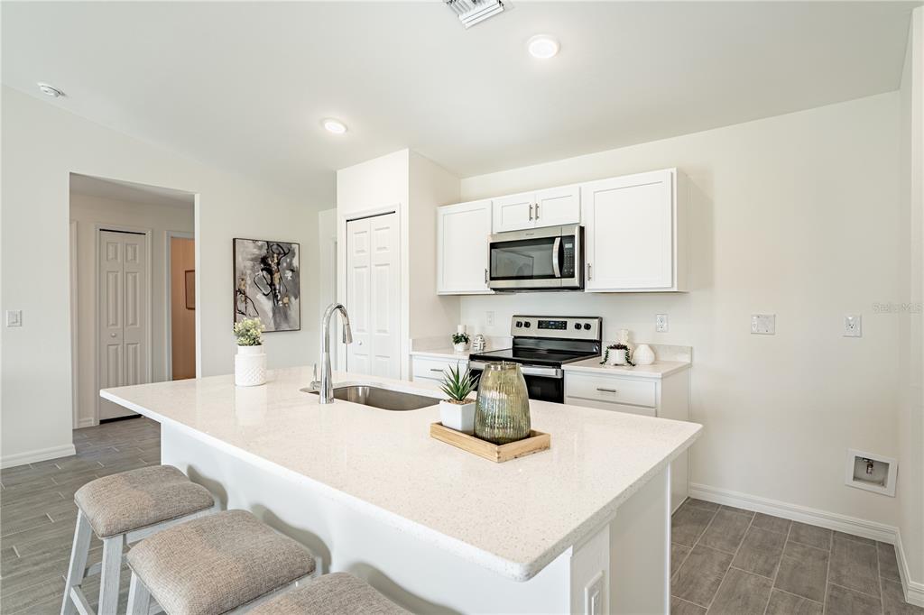 A kitchen features a white quartz island, white cabinets, stainless steel appliances, and gray flooring — 23437 STEEPLE AVENUE, PUNTA GORDA, FL