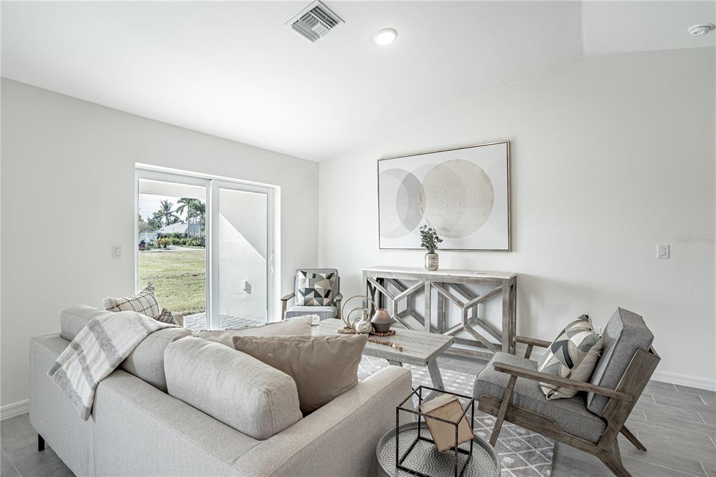 A living room features a gray sofa, two armchairs, a console table, and sliding glass doors — 23437 STEEPLE AVENUE, PUNTA GORDA, FL