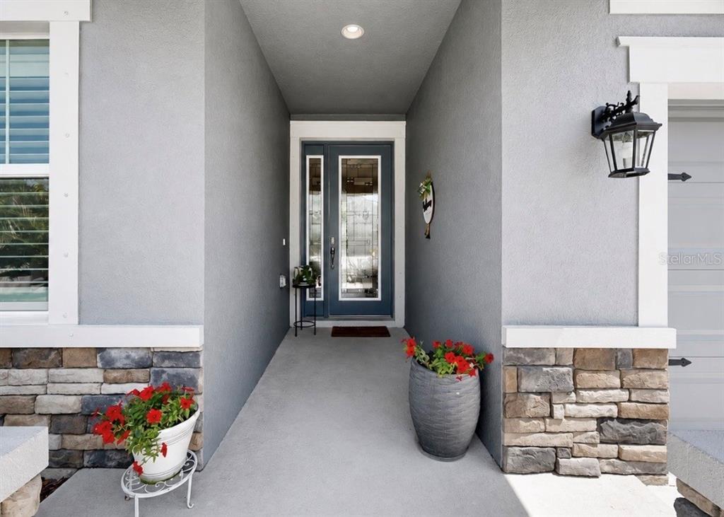A covered entryway features a gray front door, stone veneer accents, and two potted plants — 6364 ROADSTEAD COURT, APOLLO BEACH, FL