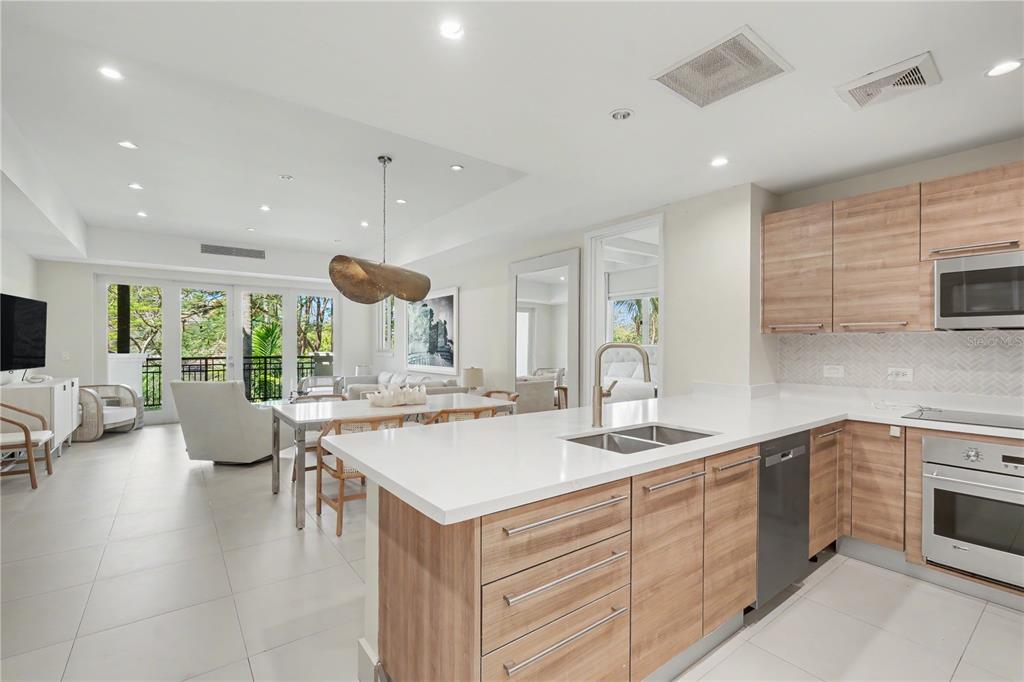 A modern kitchen with light wood cabinets and white countertops opens into a bright living area — 7000 Bahia Beach Boulvard LAS VENTANAS I UNIT 222, RIO GRANDE, PR