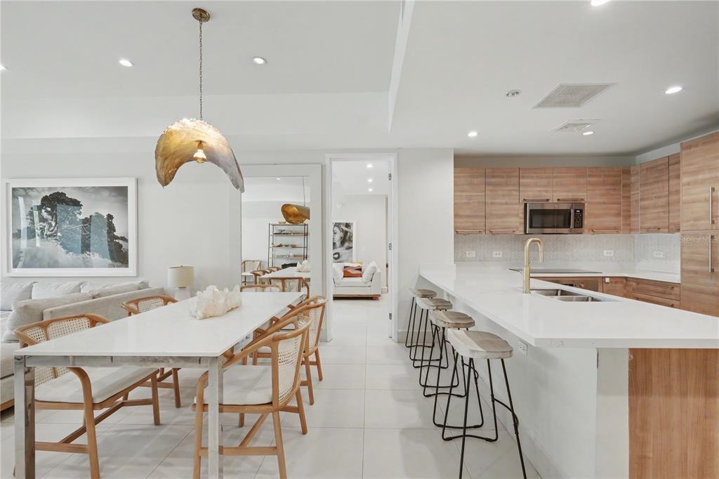 A modern kitchen and dining area feature light wood cabinetry, white countertops, and rattan chairs — 7000 Bahia Beach Boulvard LAS VENTANAS I UNIT 222, RIO GRANDE, PR