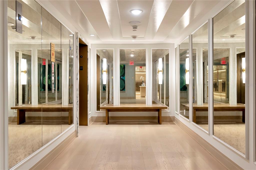 A hallway with light wood floors, mirrored walls, and wooden benches on both sides — 3101 W BAYSHORE BOULEVARD UNIT 804, TAMPA, FL