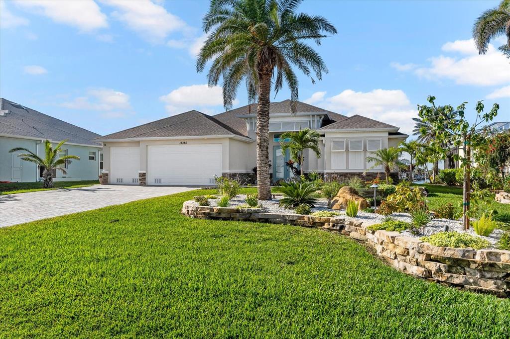 A single-story house with a white garage, a palm tree, and a stone-walled garden bed — 15380 ALSASK CIRCLE, PORT CHARLOTTE, FL