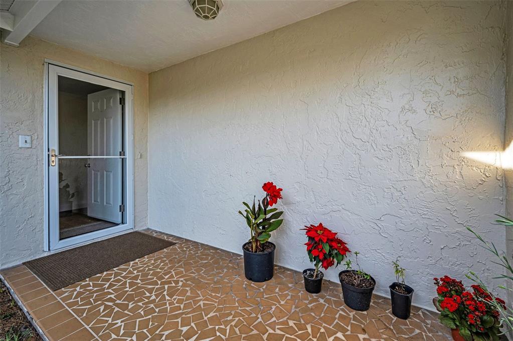 A covered porch features a mosaic tile floor, textured white walls, and several potted plants — 817 RIVERSIDE DRIVE, TARPON SPRINGS, FL
