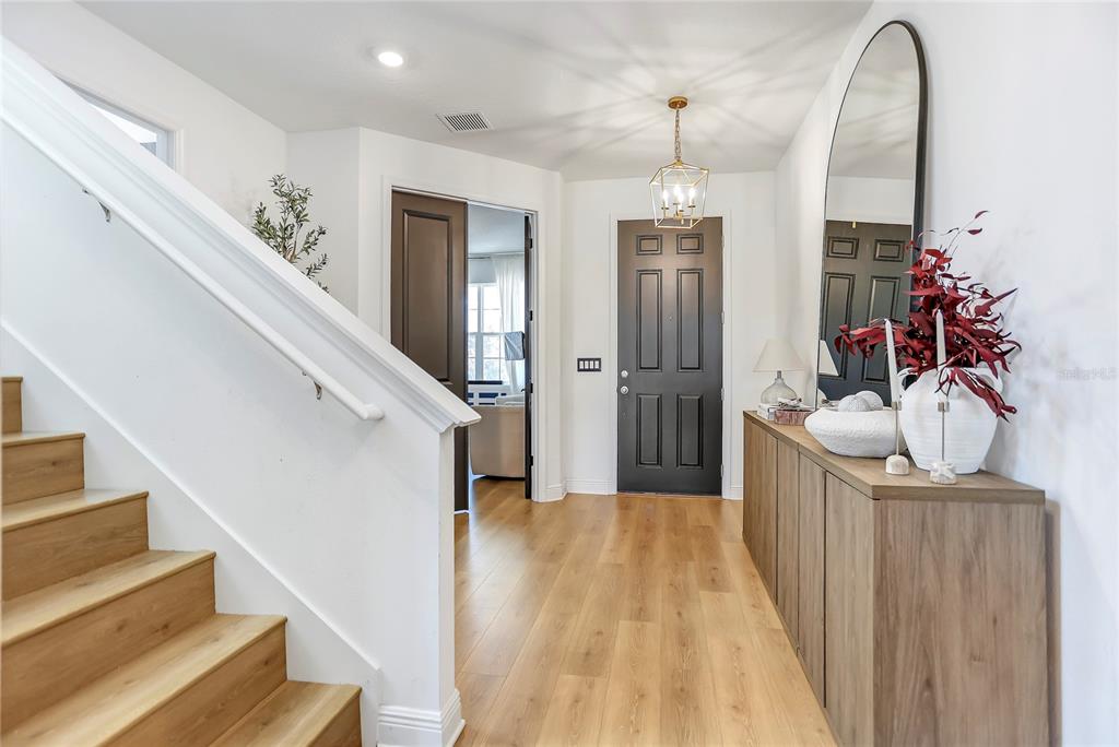 A bright entryway features light wood flooring, a staircase, a dark door, and a console table — 18907 RAWSON STREET, ORLANDO, FL