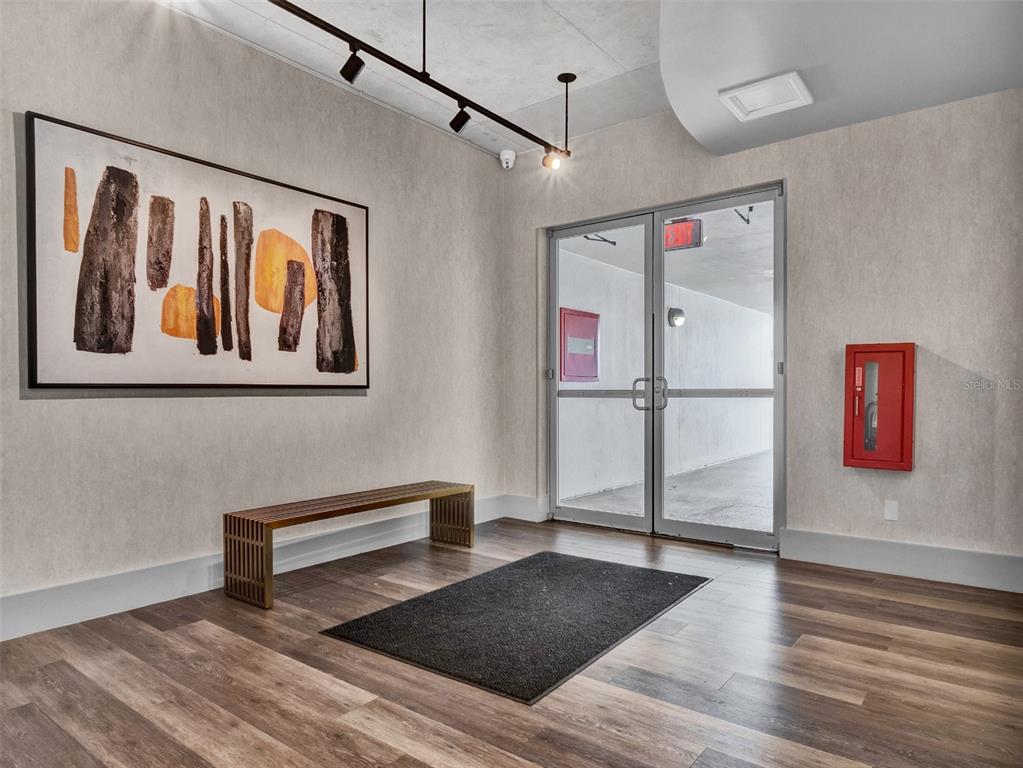 A modern entryway features wood-look flooring, a slatted bench, abstract wall art, and glass doors — 525 E JACKSON STREET UNIT P3, ORLANDO, FL