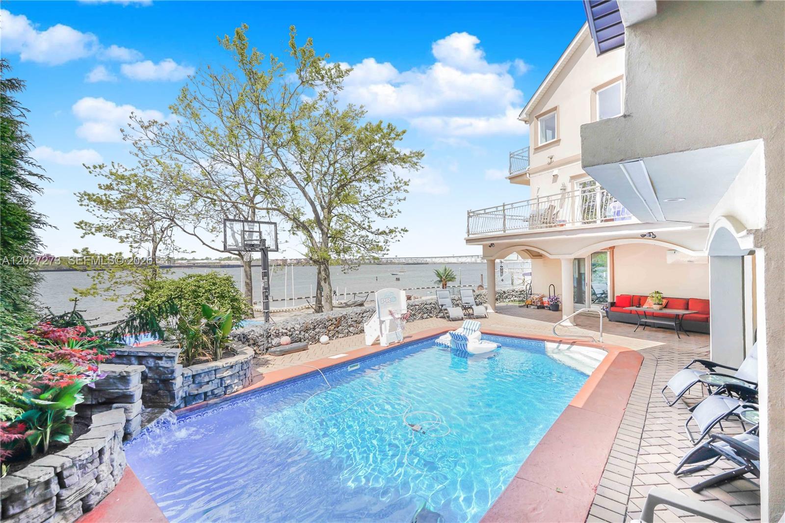 A swimming pool sits on a patio next to a house overlooking a body of water — 30 Aviva Ct, NY 10307, NY
