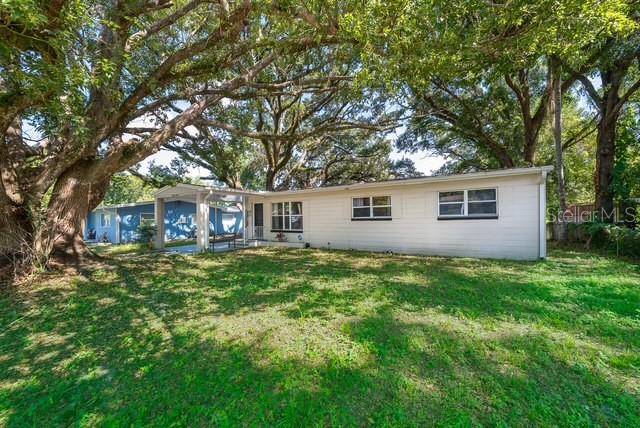 A single-story house with light siding and a carport sits under large oak trees — 3613 AMIGOS AVENUE, ORLANDO, FL