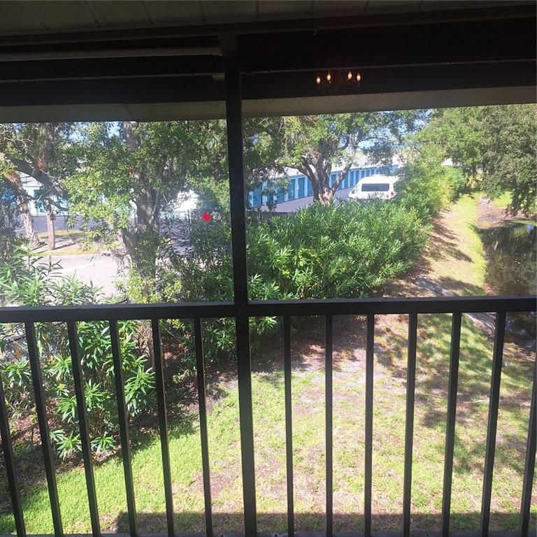 A view from a screened-in balcony overlooking a grassy area, trees, and a small pond — 2377 LAKE HEATHER HEIGHTS COURT UNIT 2377, DUNEDIN, FL