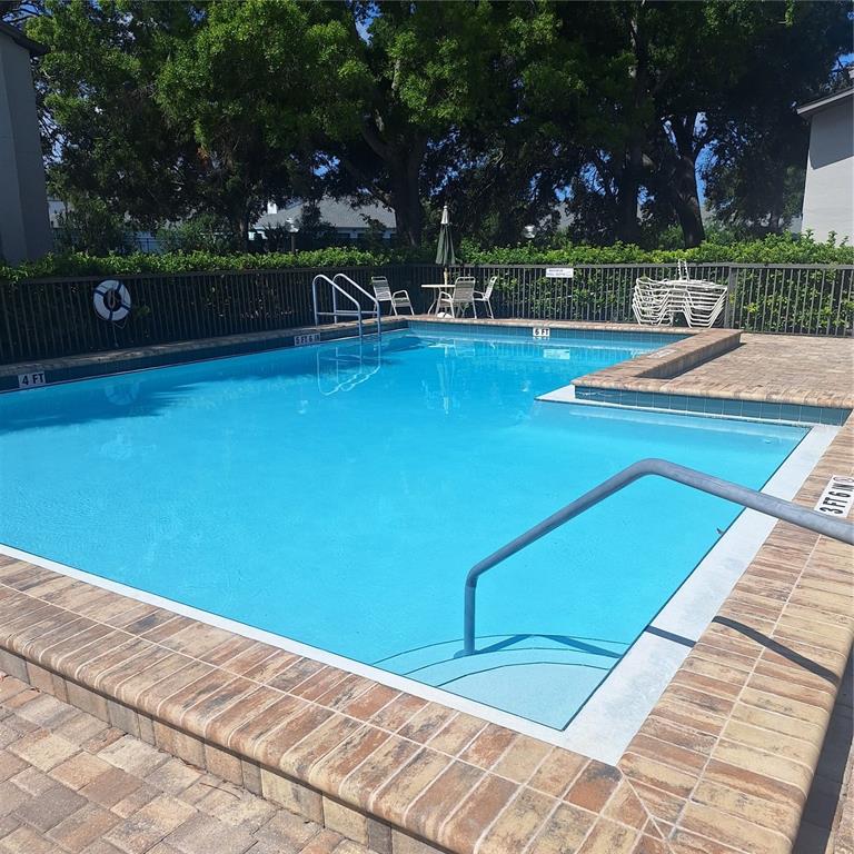 An outdoor swimming pool with a brick deck, metal railings, and a surrounding privacy fence — 2377 LAKE HEATHER HEIGHTS COURT UNIT 2377, DUNEDIN, FL