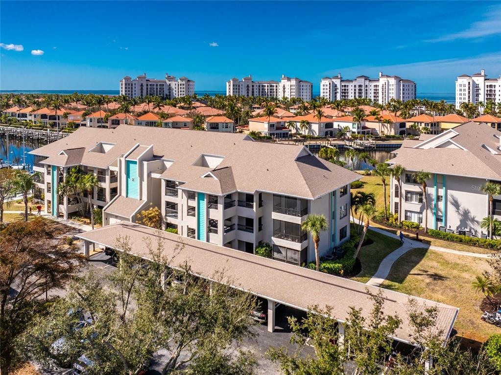 An aerial view shows a multi-story apartment complex with covered parking and surrounding palm trees — 3245 SUGARLOAF KEY ROAD UNIT 24C, PUNTA GORDA, FL