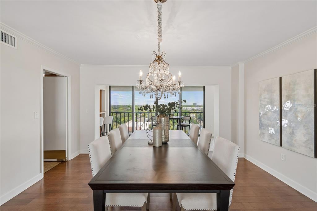 A dining room features a dark wood table, upholstered chairs, a crystal chandelier, and balcony views — 2403 S ARDSON PLACE UNIT 902B, TAMPA, FL