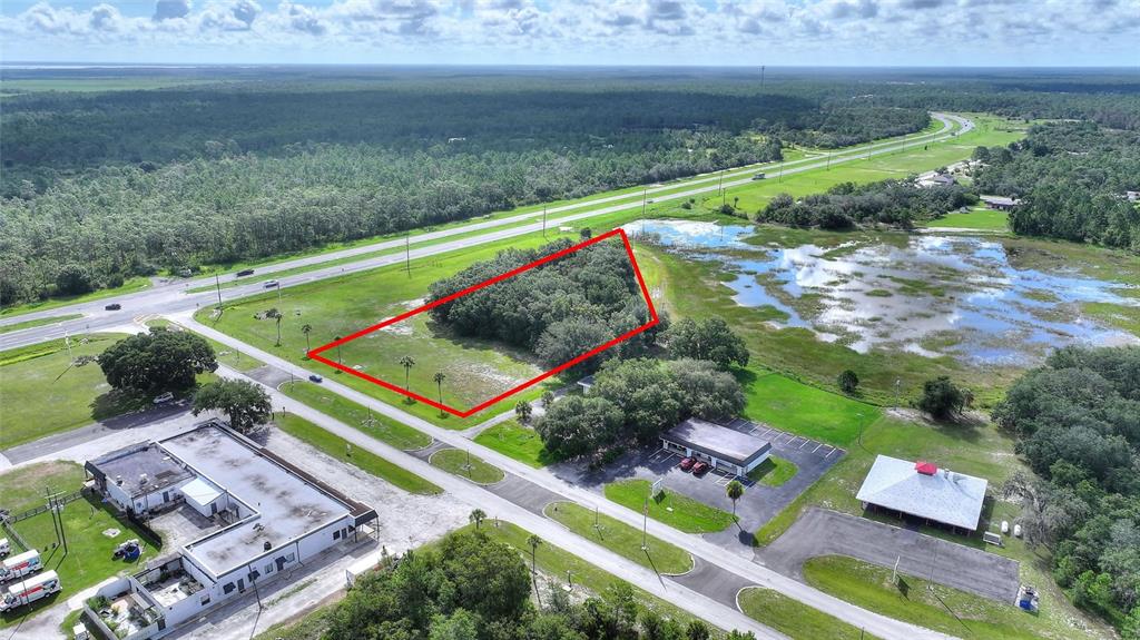 An aerial view shows a vacant, tree-covered lot outlined in red next to a highway — DELAND AVENUE, INDIAN LAKE ESTATES, FL